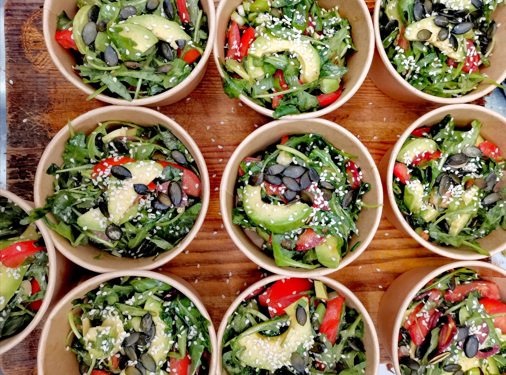 Draufsicht auf mehrere Salat-Bowls mit Avocadoscheiben und Kernen auf einer Holzfläche.